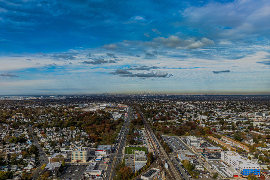 An aerial view of Valley Stream, New York, looking west along Sunrise Highway and the parallel Long Island Rail Road corridor. The scene highlights the community’s suburban neighborhoods, commercial districts, and direct transportation connections toward New York City.