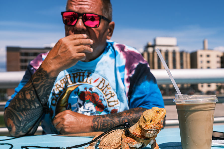 A man relaxes at an outdoor table along the Long Beach Boardwalk with a cold coffee drink and his pet bearded dragon on August 28, 2025. The unusual companion adds a playful touch to a sunny summer day in Long Beach, New York.