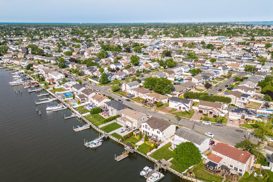 An aerial view of West Bay Shore showcases a quiet waterfront neighborhood along the South Shore of Long Island, where homes with private docks line the shoreline and residential streets extend inland toward the community center. The image highlights the hamlet's close connection to the water, its well-established neighborhoods, and its convenient location near the Great South Bay, making it an attractive place for boating, waterfront living, and suburban life.