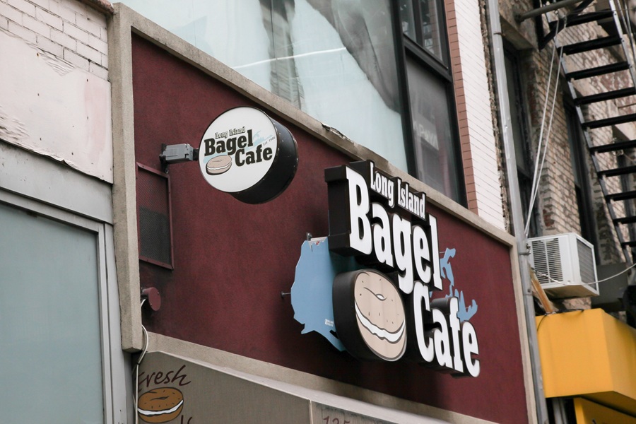 The Long Island Bagel Cafe sign hangs above Fulton Street in Lower Manhattan, highlighting one of New York's enduring culinary connections to Long Island. While the café operates in Manhattan, its name reflects the widespread reputation of Long Island-style bagels, which are celebrated for their crisp exterior, chewy texture, and longstanding role in the region's breakfast culture. File photo: Miro Vrlik Photography, licensed.