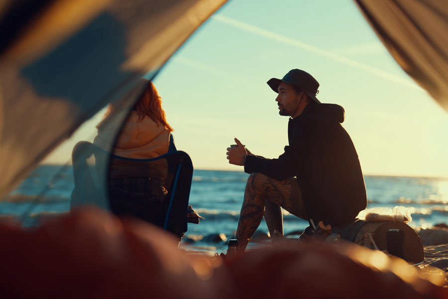 A pair of campers relax beside the ocean at sunset, capturing the peaceful experience of beach camping on Long Island. From oceanfront campgrounds to scenic coastal parks, a night under the stars offers one of the island's most memorable outdoor adventures. File photo: Gorodenkoff, licensed.