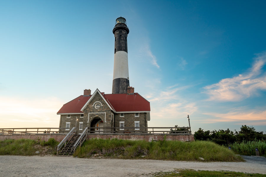 The historic Fire Island Lighthouse rises above the dunes of Fire Island National Seashore as the evening sky begins to glow with the warm colors of sunset. Built in 1858, the iconic black-and-white tower has guided mariners along Long Island's Atlantic coast for more than a century and remains one of the Island's most recognizable landmarks and popular historic attractions.