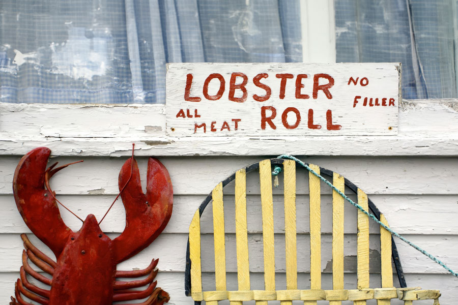 A hand-painted sign advertising fresh lobster rolls hangs outside a coastal seafood shack, reflecting the simple traditions and maritime charm that have made lobster rolls one of Long Island's most iconic waterfront foods. File photo: Christopher Seufert, licensed.