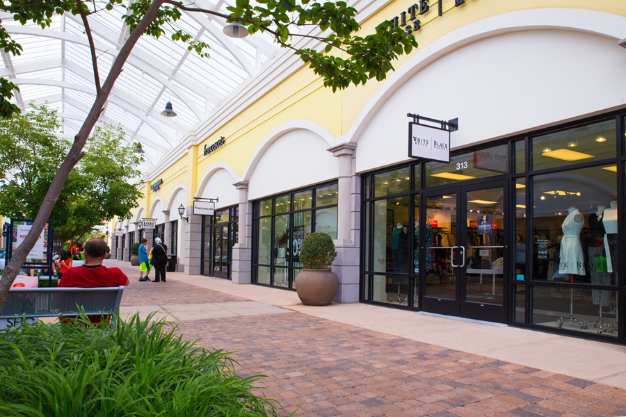 Shoppers stroll past a collection of brand-name outlet stores at Tanger Outlets Deer Park, one of Long Island's premier open-air shopping destinations. Landscaped walkways, outdoor seating, and a modern village-style design create an inviting atmosphere where visitors can browse more than 100 retail stores, enjoy dining options, and attend seasonal events throughout the year. File photo: Little Vignettes Photo, licensed.