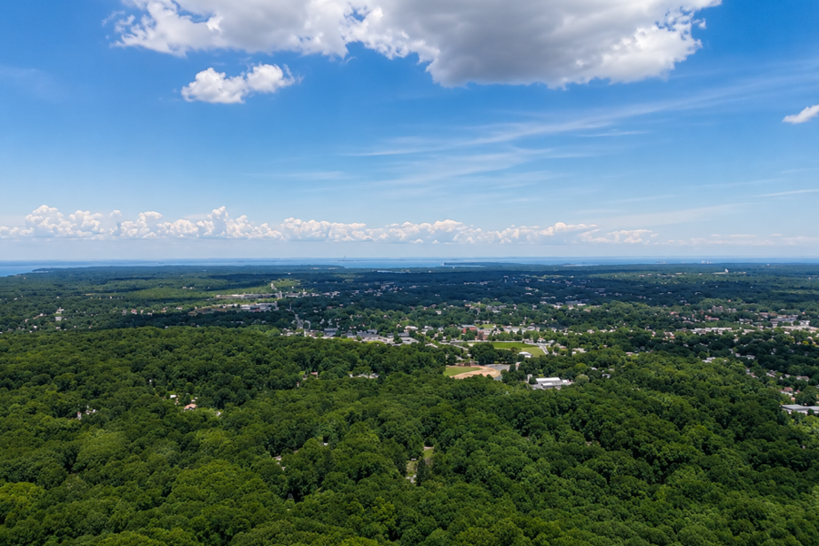 View from Jayne's Hill, the highest natural point on Long Island, looking across the wooded landscape of West Hills County Park in Huntington. Dense hardwood forest covers the surrounding hills, with suburban communities visible beyond the trees and Long Island Sound appearing in the distance on a clear day.