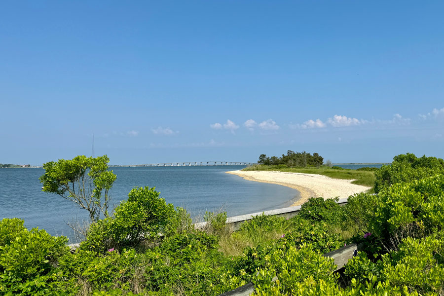 A beach along Flanders Bay near Hampton Bays, Long Island, New York, showing the bay’s calm shallow waters, sandy shoreline and coastal vegetation. The scene reflects the sheltered estuarine landscape where Flanders Bay connects the Peconic River watershed with the larger Peconic Bay system.