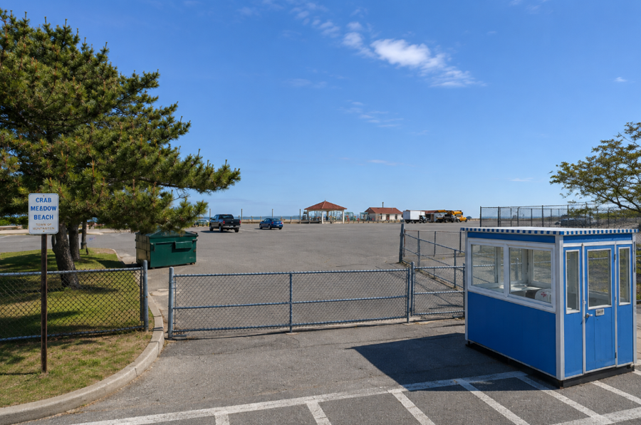 The entrance to Crab Meadow Beach in Northport, with the parking area, attendant booth and waterfront facilities visible beyond the gate. The Town of Huntington beach sits along the Long Island Sound and offers swimming, picnicking, a boardwalk and other seasonal recreation.