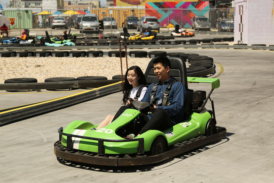 Two riders enjoy a go-kart race at Coney Island Raceway in Brooklyn, New York, with other racers circling the track in the background. The attraction is part of the amusement offerings at Coney Island and provides a classic outdoor karting experience.