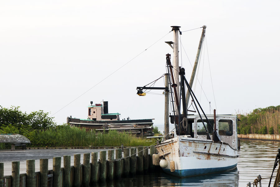 Historic boats sit along the waterfront at the Long Island Maritime Museum in West Sayville, overlooking the Great South Bay. The scene reflects Long Island’s shipbuilding, fishing and oyster-harvesting traditions. The museum preserves these maritime connections through its historic vessels, waterfront buildings and exhibits.