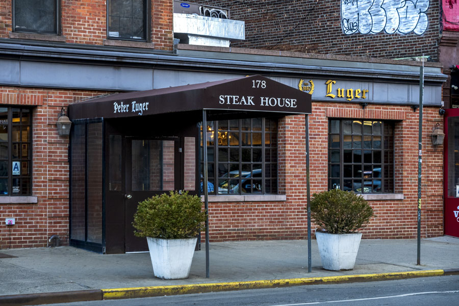 The historic Peter Luger Steak House in Williamsburg, Brooklyn, features a classic brick facade and its distinctive entrance awning. Founded in 1887, the restaurant is also represented on Long Island by its Great Neck location.