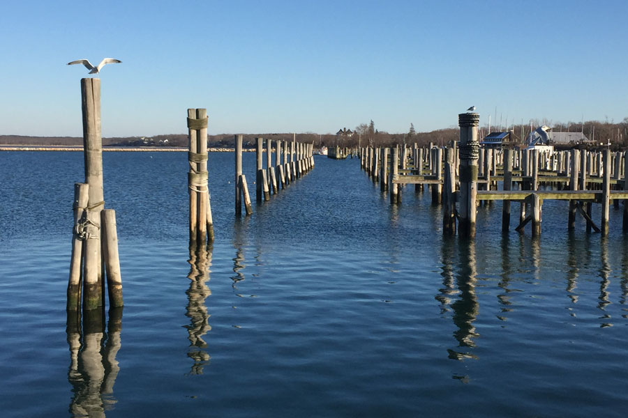 View across the calm waters of Shinnecock Harbor, where rows of wooden pilings and docks reflect the area’s longstanding maritime character. The harbor remains an important working waterfront for recreational boating, fishing and marine activity near Shinnecock Inlet and Hampton Bays.