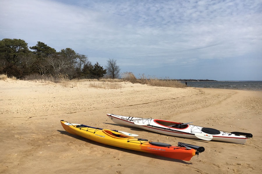 Two kayaks resting on the sandy shoreline of Indian Island County Park in Riverhead, Long Island, New York. The calm waters of the Peconic River and Flanders Bay make the park a popular setting for kayaking, fishing and waterfront recreation.