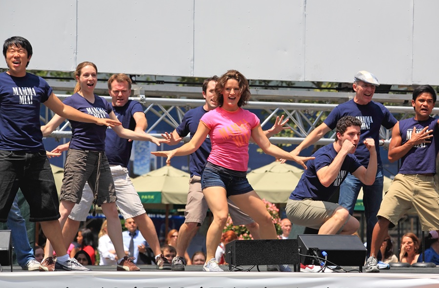 Cast members from Mamma Mia! perform an energetic musical number during an outdoor stage performance. The image captures the lively spirit of Broadway-style theater and live performing arts that audiences can enjoy at venues across Long Island.