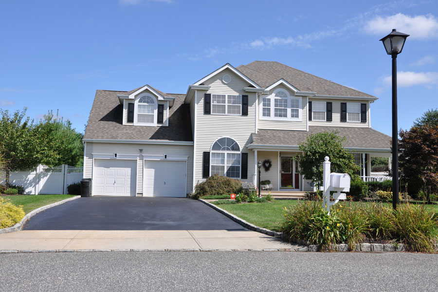 A suburban single-family home with a two-car garage and landscaped front yard illustrates the type of housing tracked in Long Island’s residential real estate market. August 2026 data shows median single-family home prices rose in both Nassau and Suffolk counties even as closed sales declined.