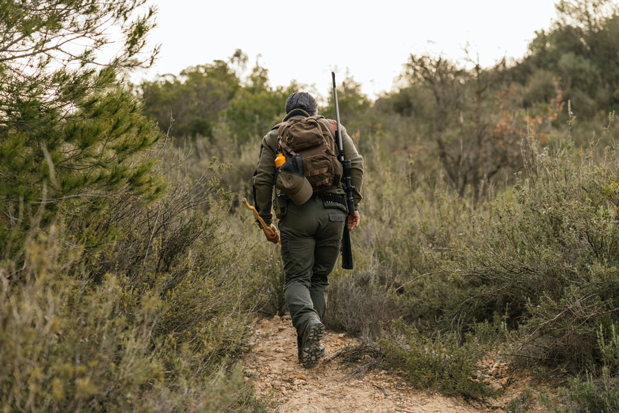 A hunter carrying hunting equipment and a backpack walks along a wooded trail. Long Island offers regulated public hunting opportunities on designated state and county lands, primarily in Suffolk County, where hunters must follow applicable licensing, permit, seasonal and property-specific requirements.