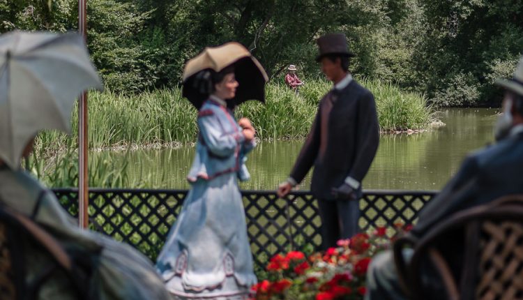Life-size sculptures of elegantly dressed figures, including a woman with a parasol and a man in a top hat, create a garden-party scene beside a pond at Old Westbury Gardens in Old Westbury, New York. A fishing figure appears in the background of the Johnson sculpture exhibition, photographed on July 22, 2017, evoking the leisurely estate life associated with Long Island’s Gold Coast era. File photo: Jay Gao, licensed..